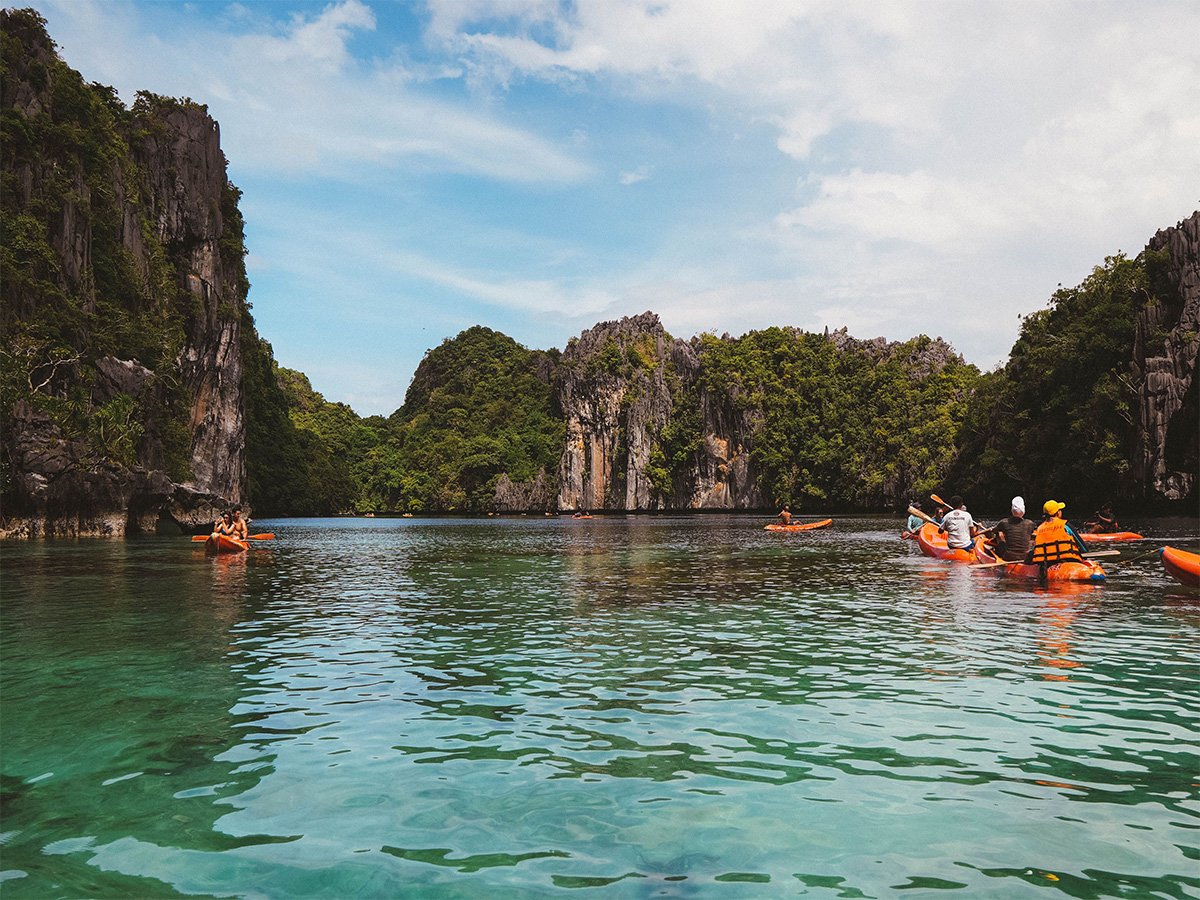 Kayakers on turquoise water surrounded by limestone cliffs in El Nido, Palawan, Philippines