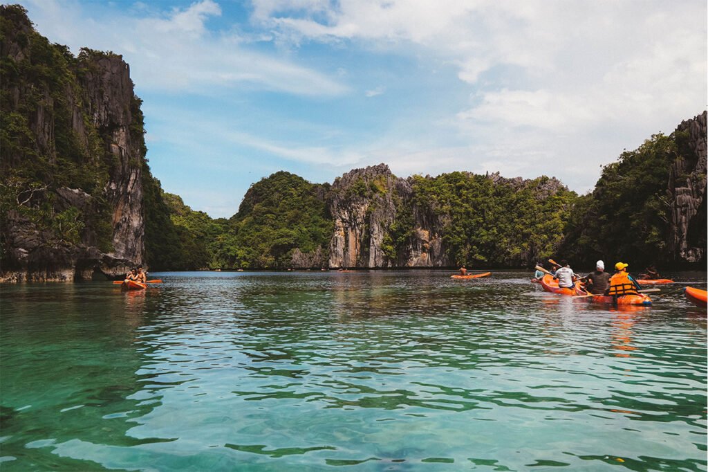 Kayakers on clear lagoon water surrounded by limestone cliffs