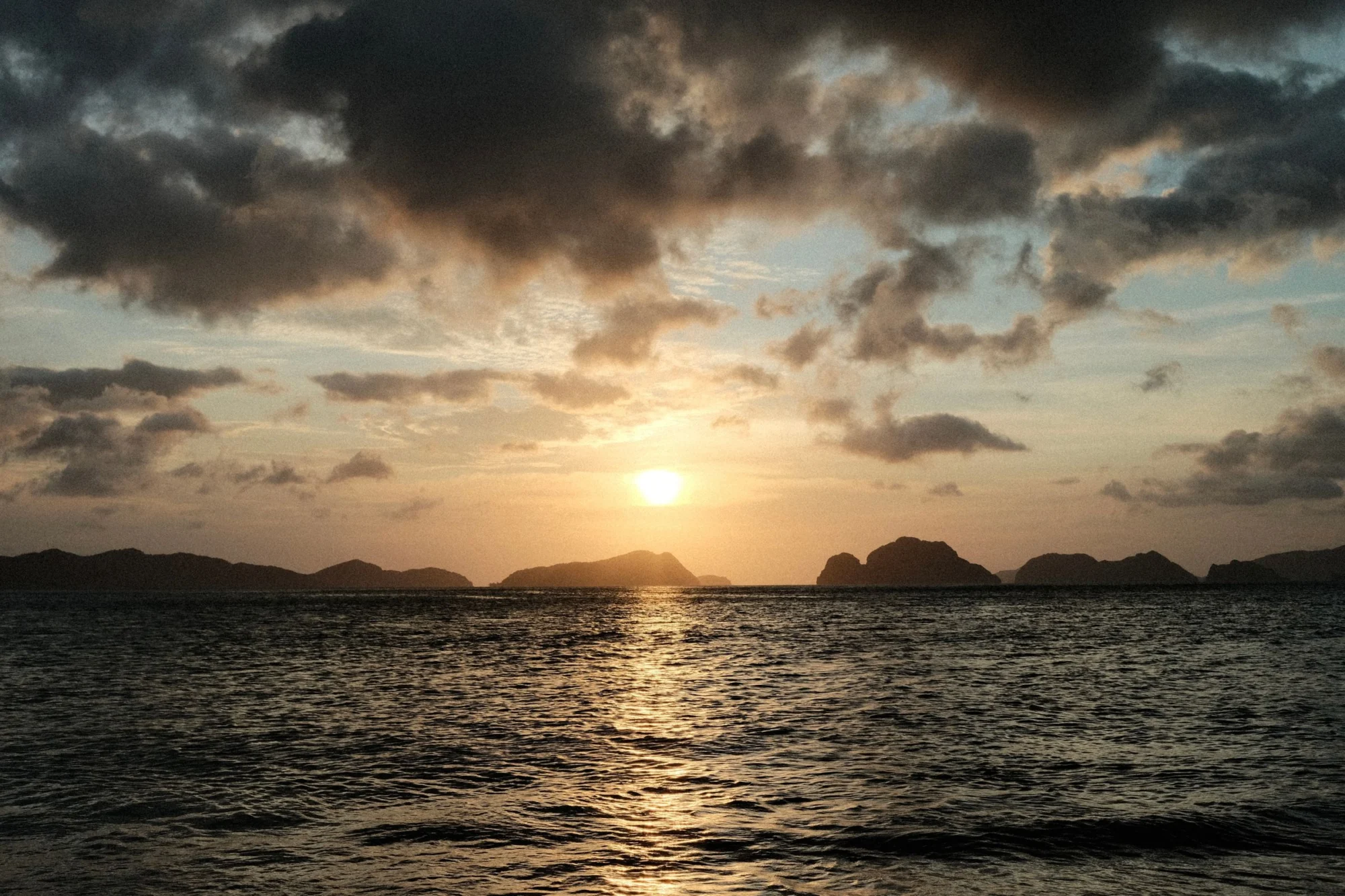 Sun setting over the sea and silhouetted limestone islands in El Nido