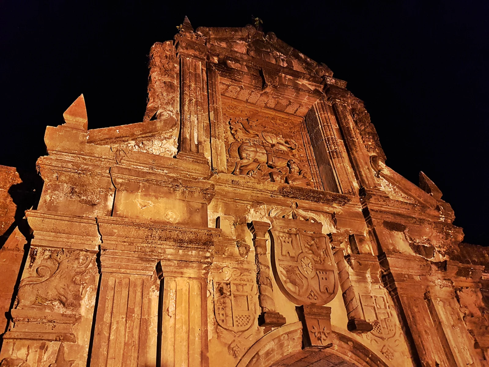 Illuminated carved stone gateway of Fort Santiago against the night sky