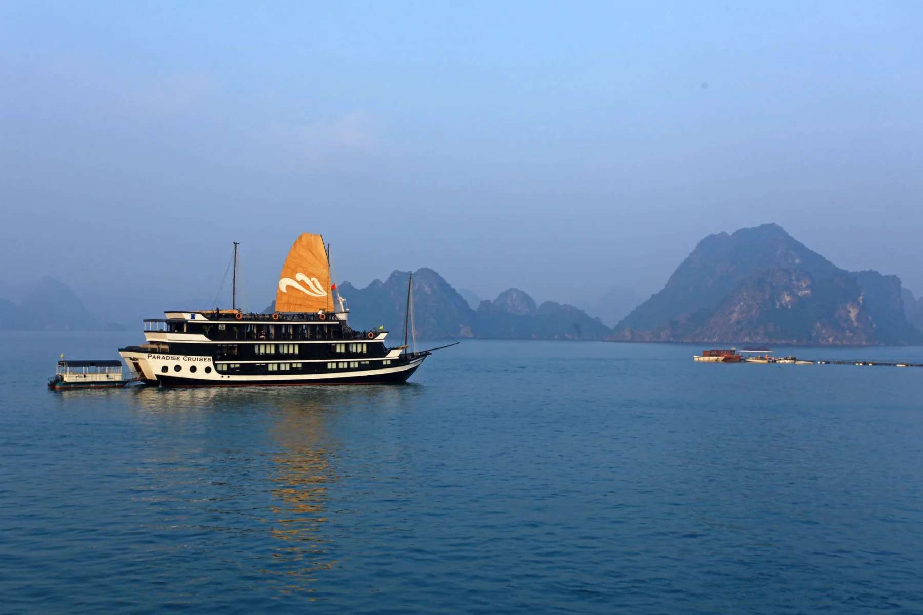 Cruise boat with an orange sail among limestone islands in Ha Long Bay