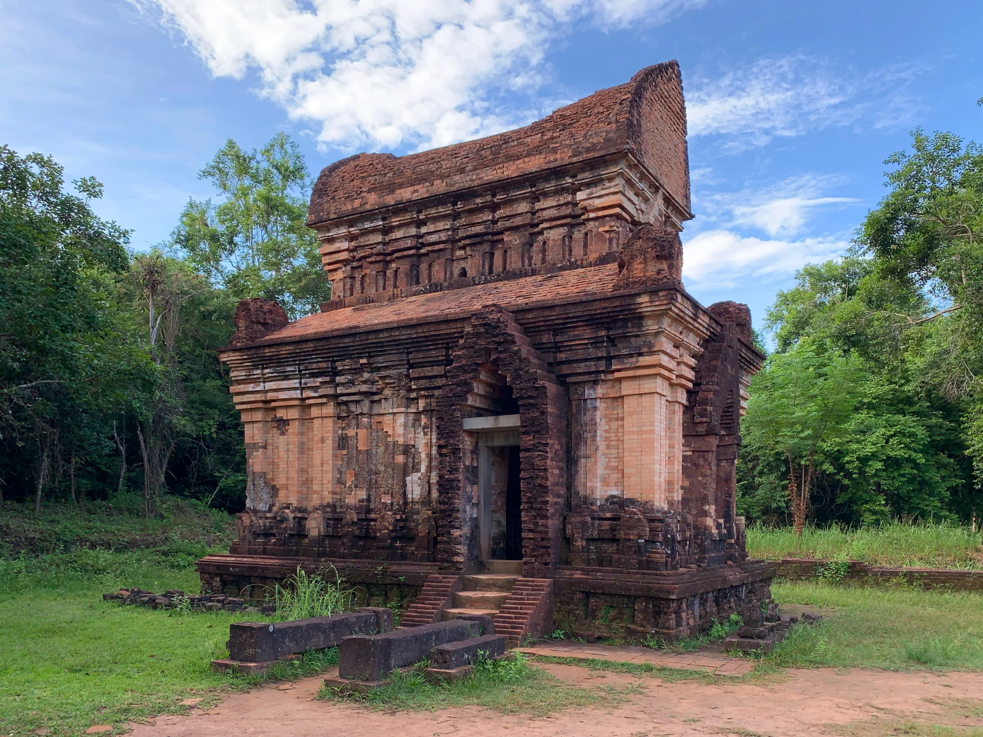 Red brick Temple E7 at My Son Sanctuary surrounded by trees under a blue sky
